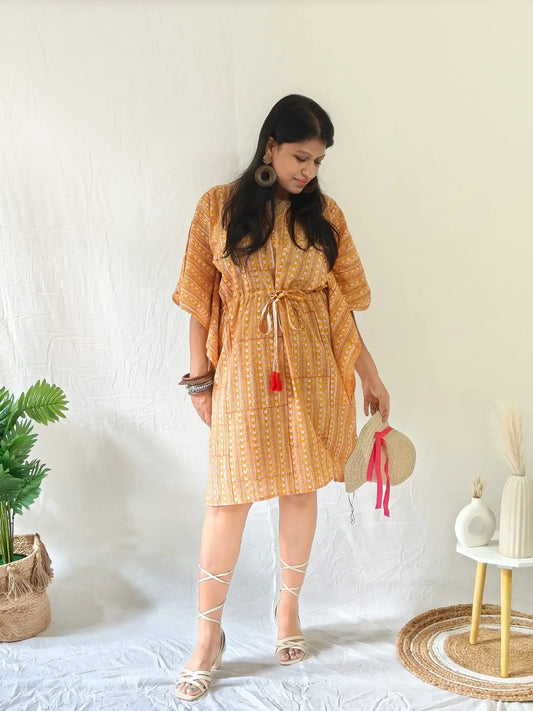 Model in orange block print kaftan with beach accessories, straw hat, and open sandals.