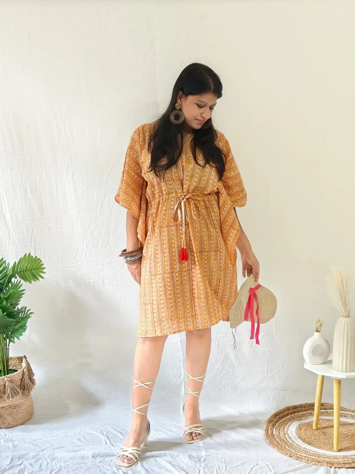 Model in orange block print kaftan with beach accessories, straw hat, and open sandals.

