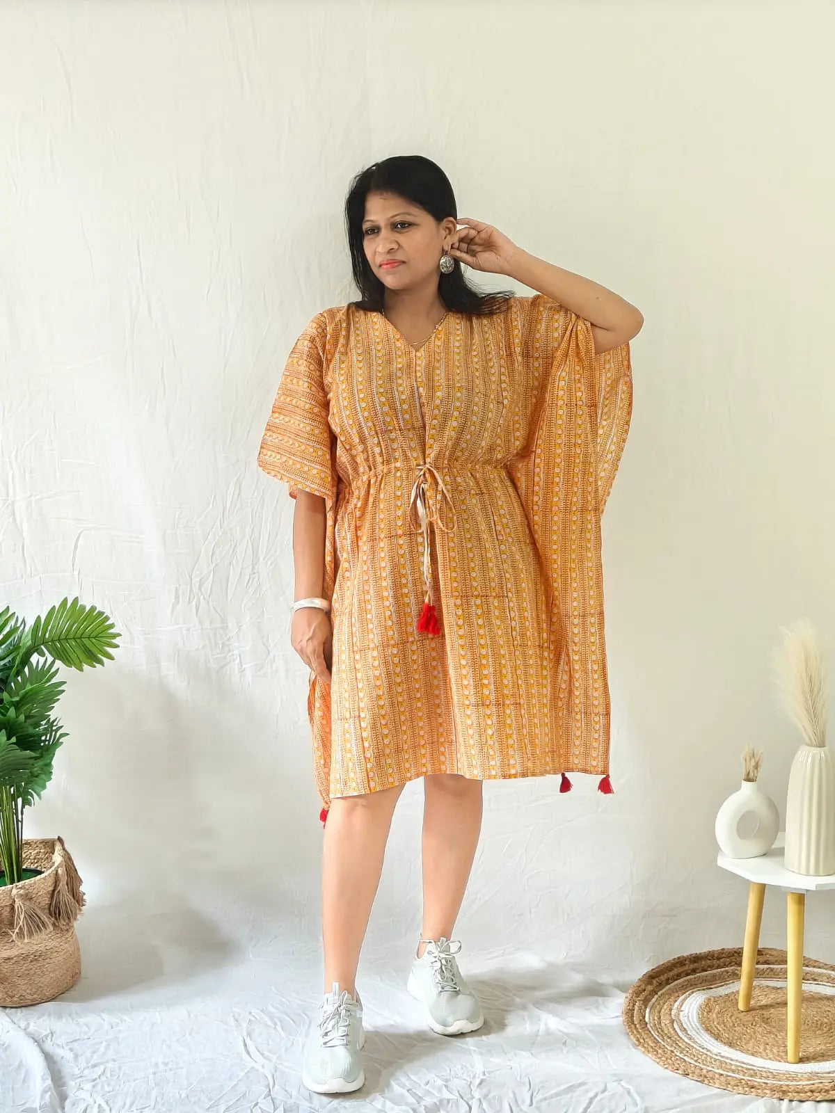 Model in orange kaftan styled with white sneakers and minimal jewellery for a laid-back look.