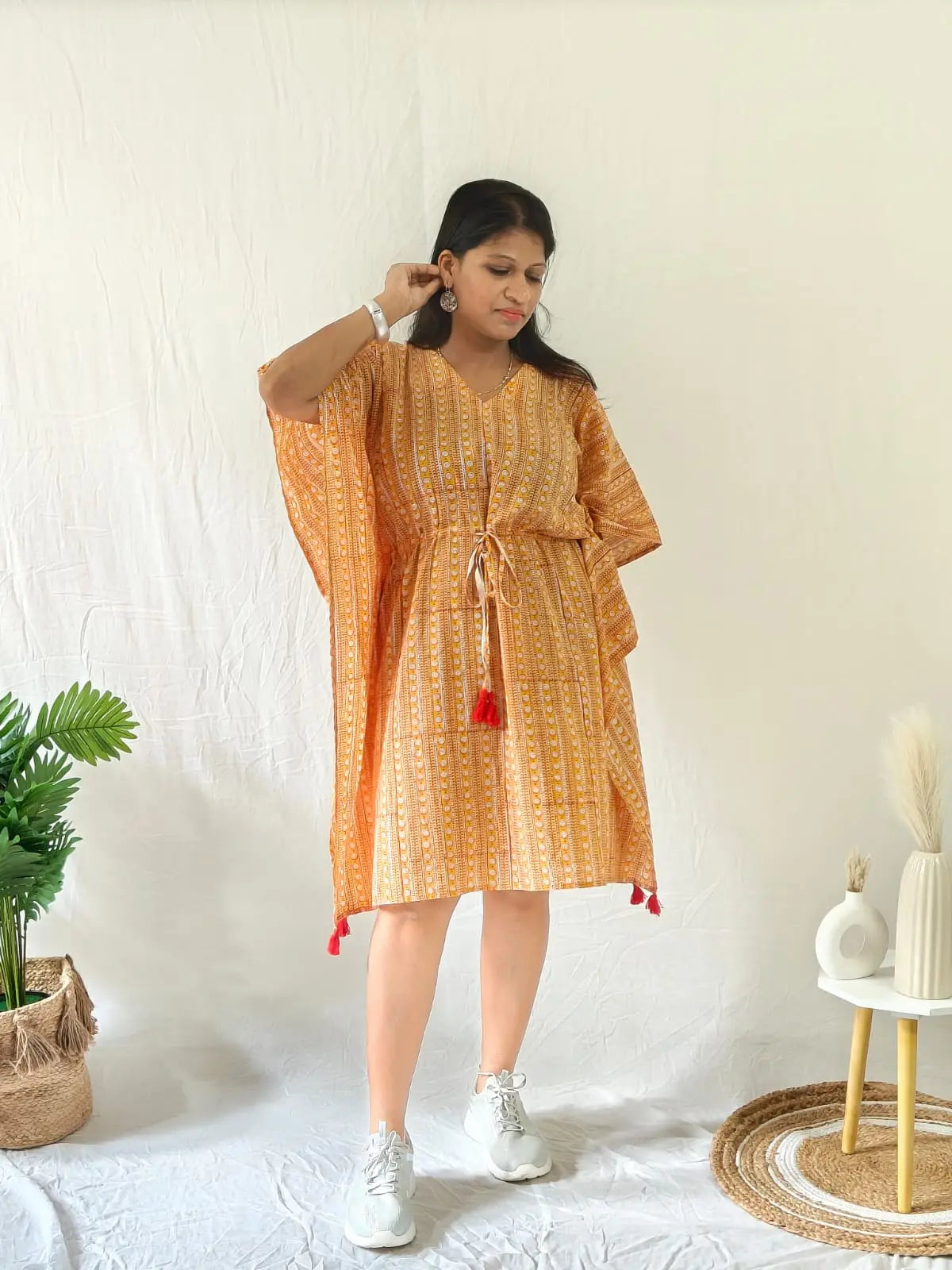 Model in orange kaftan styled with white sneakers and minimal jewellery for a laid-back look.