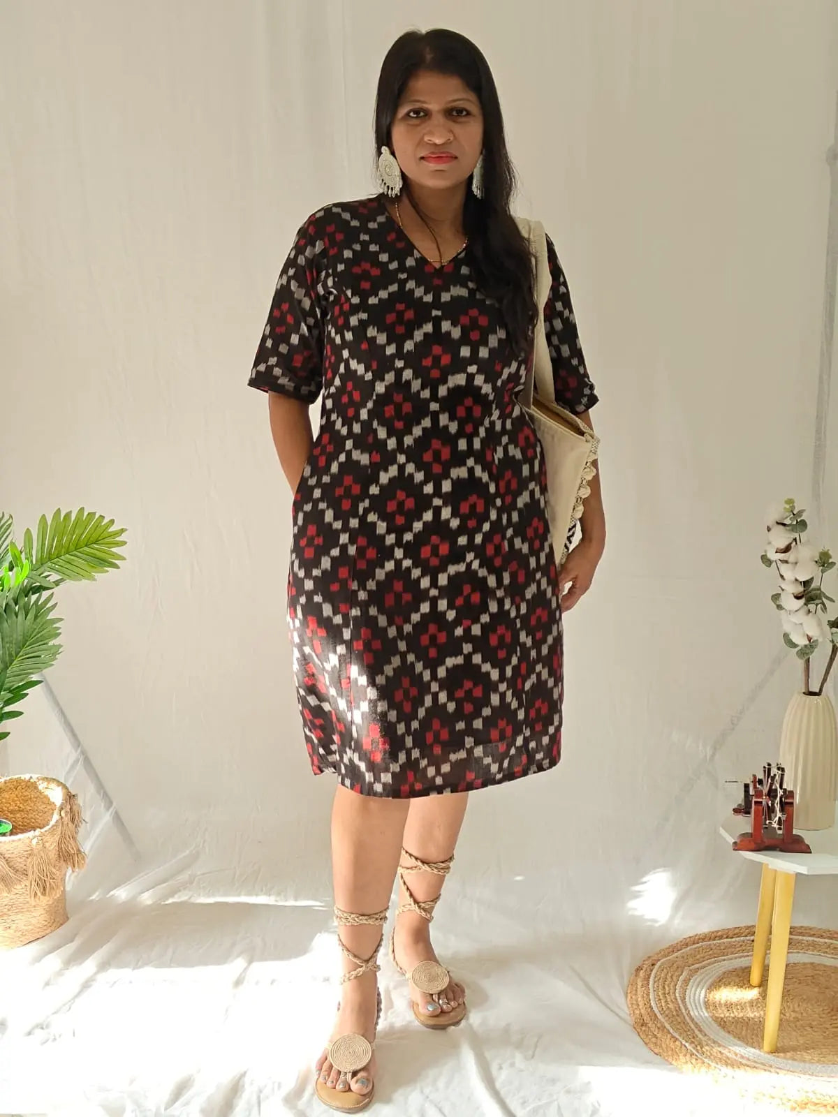 Front view Black ikkat dress with tie-up sandals, earrings, and sling bag.