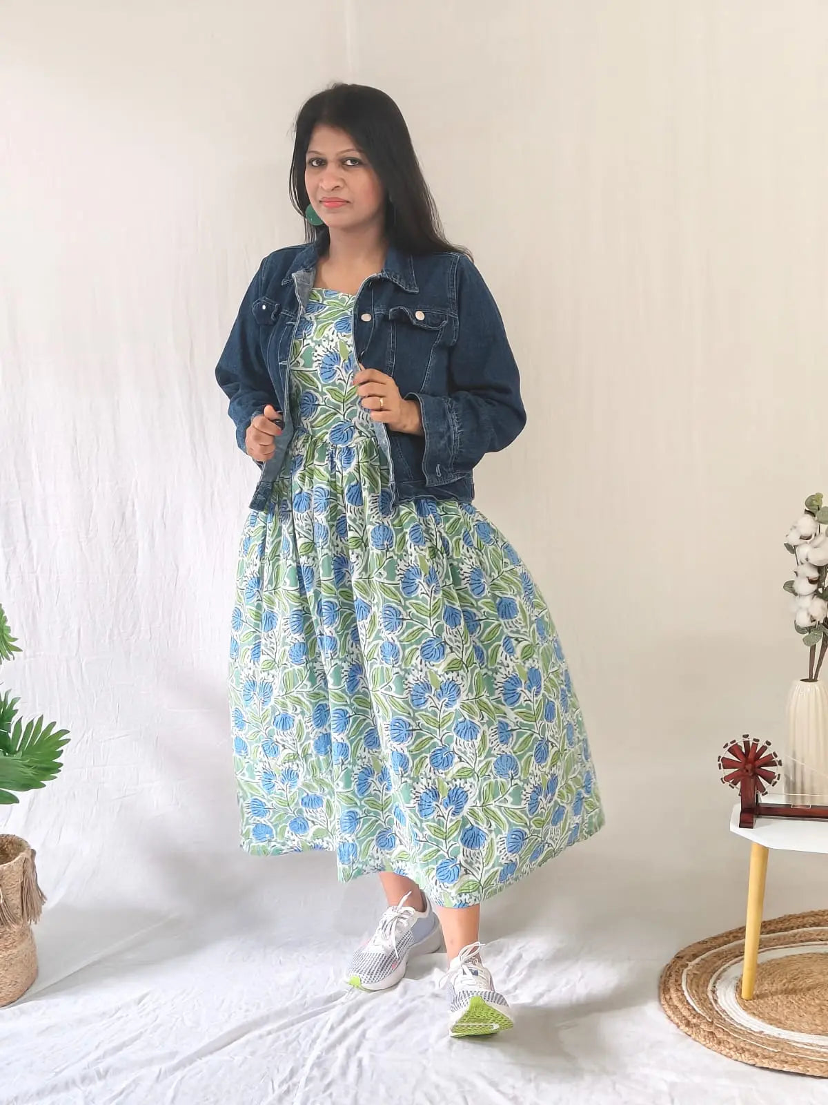Front view of spaghetti strap floral dress styled with denim jacket and casual shoes.