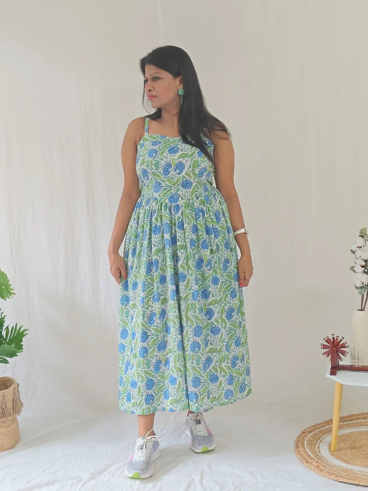 Front view of spaghetti strap floral dress styled casually with white sneakers.