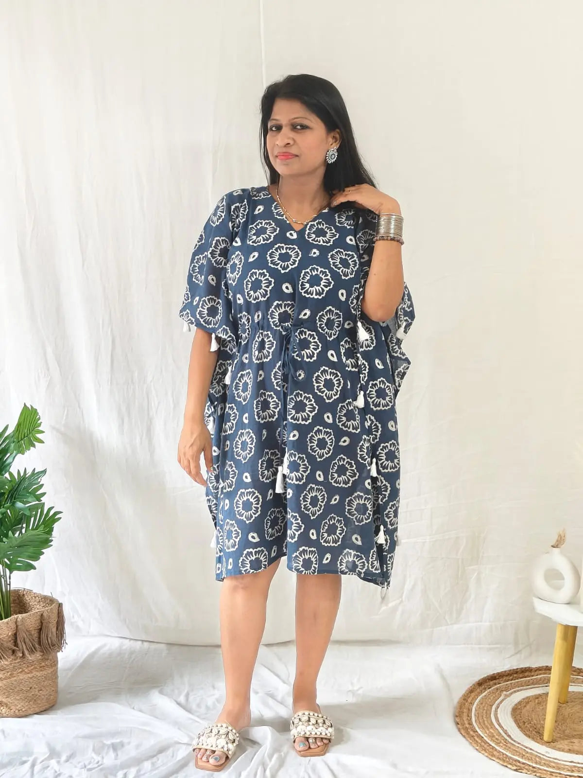 Front view of blue block print kaftan with tassels, styled for beach with seashell flats and jewellery.