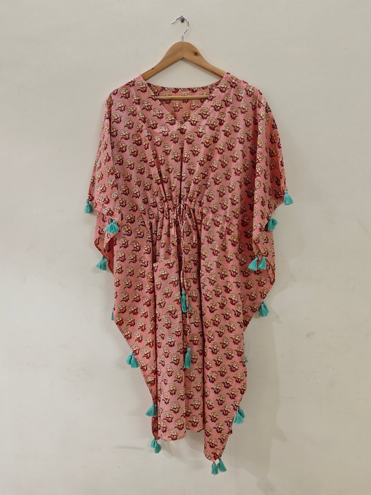 Peach kaftan hanging on hanger, front view.







