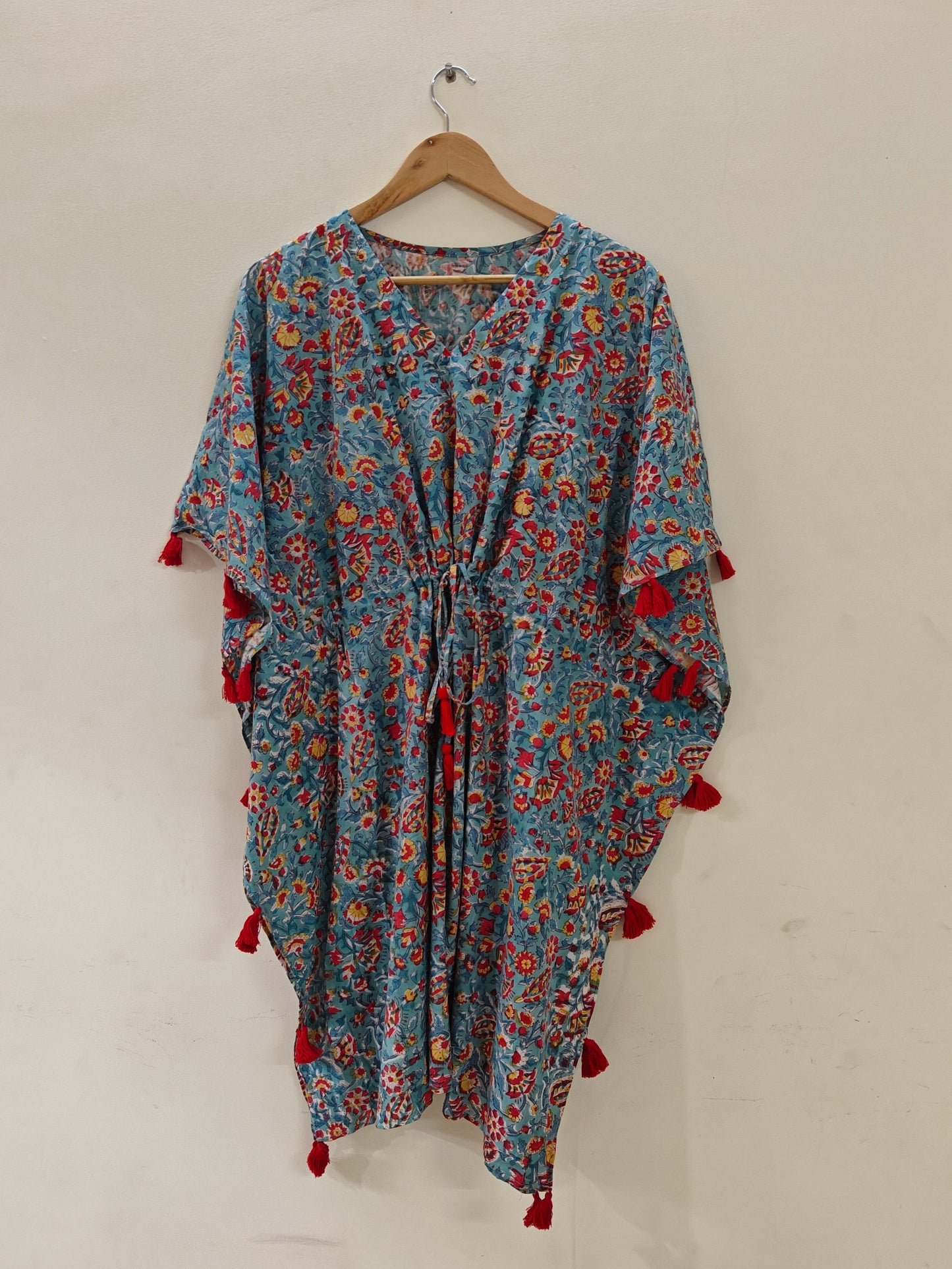 Floral patterned dress with red tassels on a hanger against a white wall